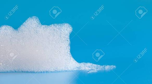 White soap bubbles foam on blue background. Suds shower texture macro view photo, shallow depth of field